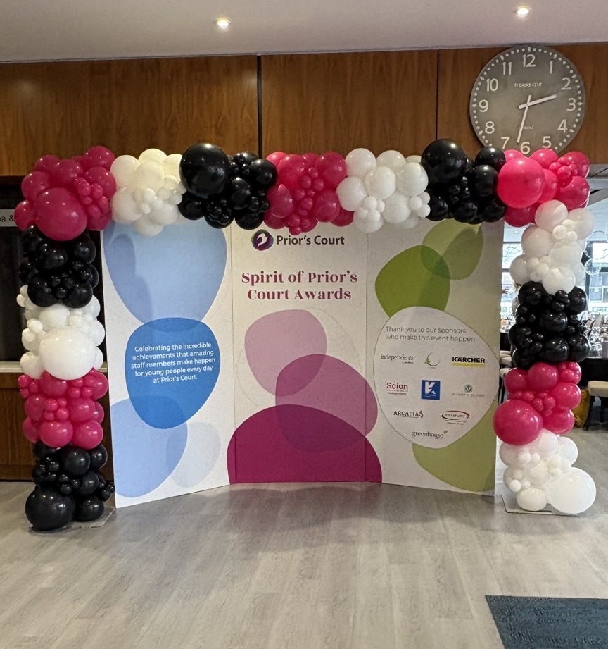 Balloon columns and a garland in magenta, black and white framing the Spirit of Prior’s Court Awards backdrop.