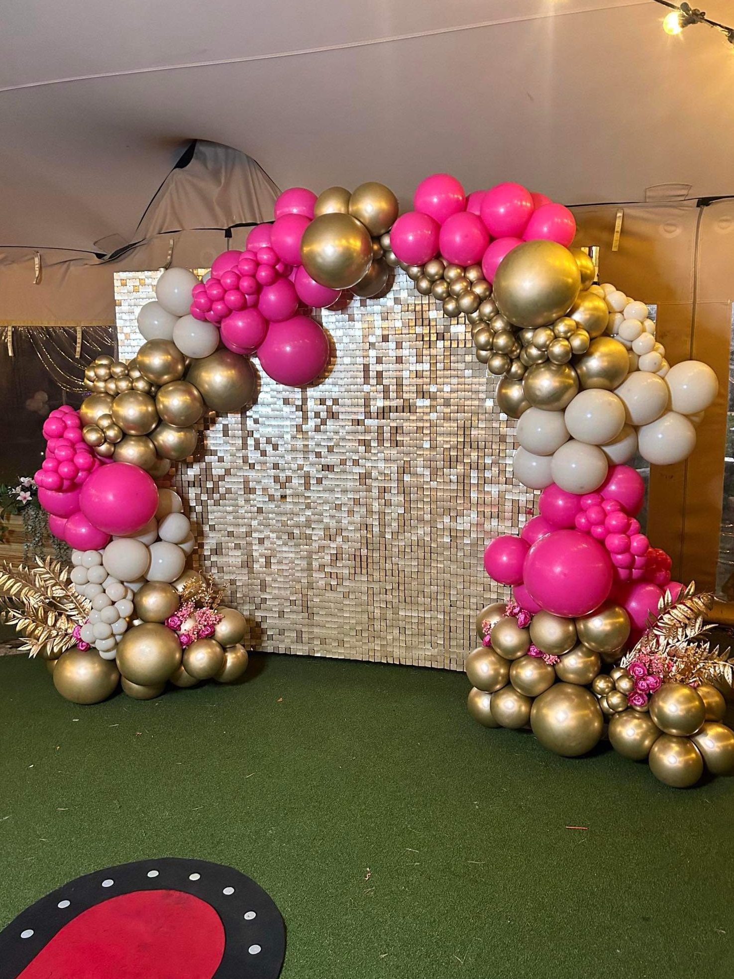 A gold sequin wall wrapped in an organic garland of hot pink, chrome gold and white balloons with gold foliage.
