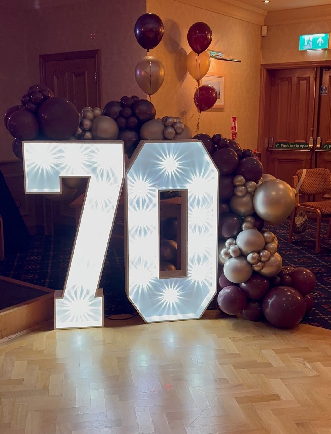 Giant light-up LED 70 numbers styled with burgundy, champagne and gold balloons in a function room.