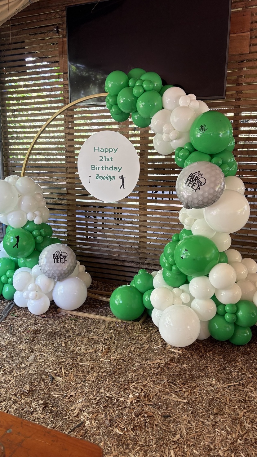 A green and white balloon welcome display around a gold hoop with a personalised Happy 21st Birthday sign.